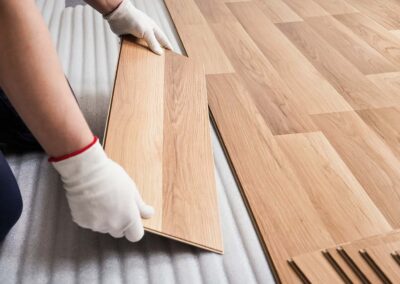 Installing laminated floor, detail on man hands fitting wooden tile, over white foam base layer